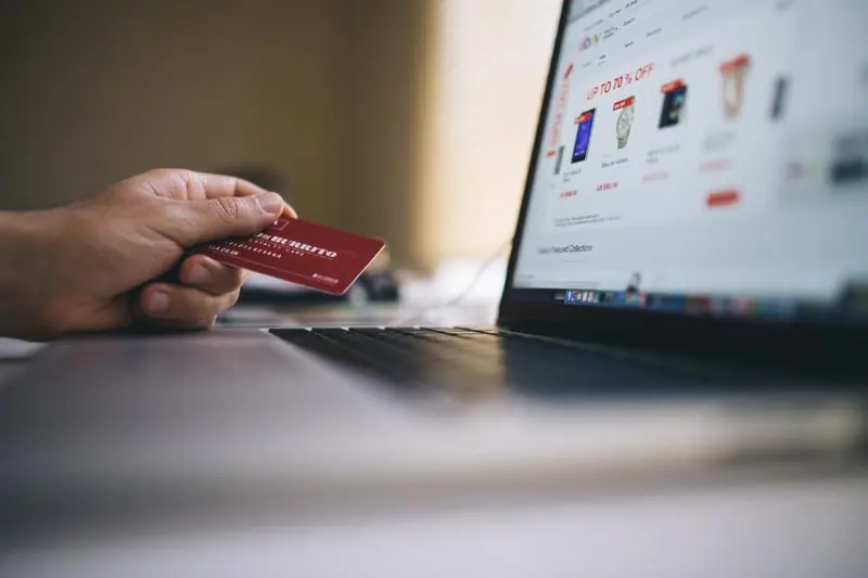 Mano con una tarjeta de crédito frente a una notebook con una tienda online abierta